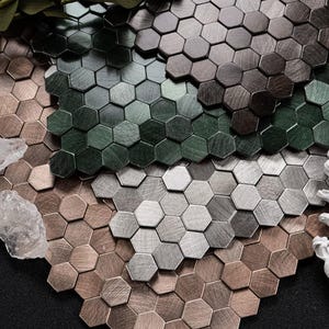 May include: A close-up of a collection of metallic hexagonal tiles in various shades of brown, gray, and green. The tiles have a brushed metal finish, creating a textured appearance. The arrangement suggests a decorative or design element.