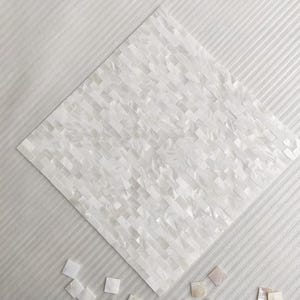 May include: White mother-of-pearl mosaic tile sheet. The tile is made of small, rectangular pieces arranged in a brick pattern. Several loose tiles are scattered around the main sheet. The background is a textured, white surface.
