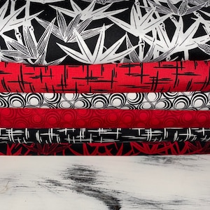 Könnte beinhalten: Ein Stapel aus vier Stoffresten mit verschiedenen Mustern. Der oberste Rest ist schwarz mit weißen stilisierten Bambusblättern. Der zweite Rest ist rot mit schwarzen Kreuzlinien. Der dritte Rest ist weiß mit schwarzen Kreisen. Der unterste Rest ist rot mit schwarzen Kreuzlinien.