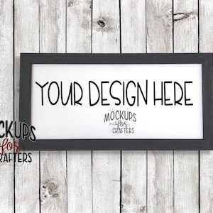 Könnte beinhalten: Ein schwarzer rechteckiger Rahmen mit weißem Hintergrund und dem Text "YOUR DESIGN HERE" in Schwarz. Der Rahmen hängt an einer weißen Holzwand.