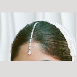 Könnte beinhalten: Eine silberne und klare Kristall-Haarkette mit einem tropfenförmigen Anhänger. Die Kette wird im Haar getragen, wobei der Anhänger auf der Stirn ruht.