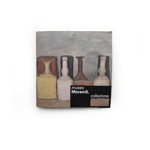 May include: A painting of four bottles in muted tones of yellow, white, and brown, set against a gray background. The artwork features the text "Museo Morandi, collezione" on a black label.