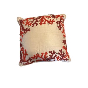 May include: Ivory square decorative pillow with coral-like embroidery in shades of red and burgundy. The embroidery is accented with small silver beads, creating a textured border design. A stylish accent for any room.