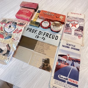May include: A collection of vintage ephemera, including a box of chalk crayons, AICO Typewrite inserts, Scotch tape, and Old English tobacco tins. Also included are Texaco maps, a shoe advertisement, and metal nameplates with engraved text.