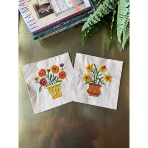 May include: Two embroidered floral patches. One features orange and red flowers in a yellow basket, the other has yellow flowers in an orange basket. Both are on a white background.