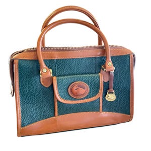 Bolso bandolera Dooney & Bourke de piel verde bosque y tostado con asas superiores, detalles dorados y bolsillo frontal tipo cartera.