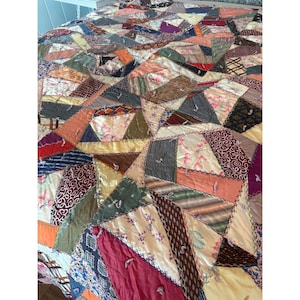 May include: A patchwork quilt with a variety of fabrics in a geometric pattern. The quilt features a mix of colors, including pink, orange, green, and purple. The quilt is made of various textures and patterns.