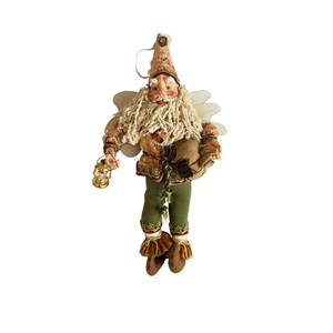 May include: A whimsical Christmas ornament depicting a fairy-like figure with a long, cream-colored beard and wings. The figure wears a patterned hat and jacket, green pants, and brown boots. It holds a golden lantern and a sack.