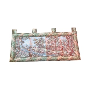 May include: A rectangular tapestry featuring a pastoral scene with trees, a river, and figures. The tapestry has a green and cream border with loops at the top for hanging. The color palette includes shades of green, cream, pink, and blue.