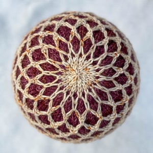 May include: A close-up of a crocheted hat with a geometric pattern in shades of burgundy and cream.