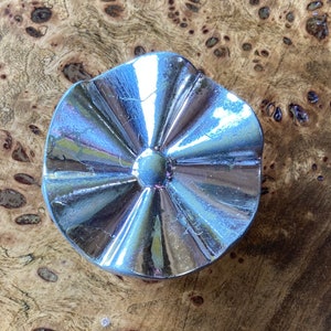 Puede incluir: Un pomo decorativo plateado con un diseño de estrella. El pomo tiene una superficie lisa y reflectante y un centro ligeramente elevado.