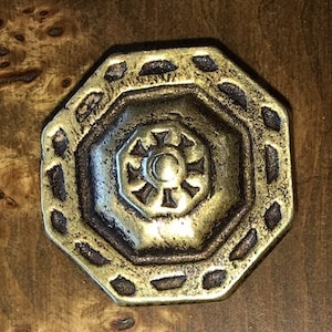May include: Octagonal brass knob with a decorative design. The knob has a raised centre with a starburst pattern and a surrounding border of small, raised squares.