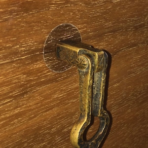 May include: A brass latch with a decorative, ornate design. The latch is attached to a wooden surface.