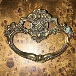 May include: A brass drawer pull with an ornate design. The pull has a heart shape and a decorative centre piece.