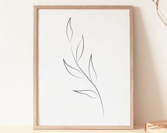 May include: A framed minimalist line drawing of a leaf branch in a light wood frame on a beige surface with a vase of dried grasses and a book.
