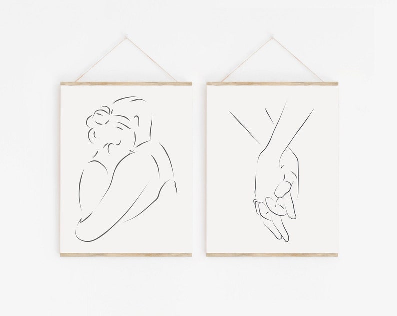 May include: Two minimalist line art prints depicting a couple embracing and holding hands. The prints are framed in a light wood frame and hung on a white wall.