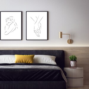 May include: Two black framed line art prints depicting a couple embracing and two hands holding each other. The prints are hanging on a white wall above a black headboard bed with a yellow throw pillow.