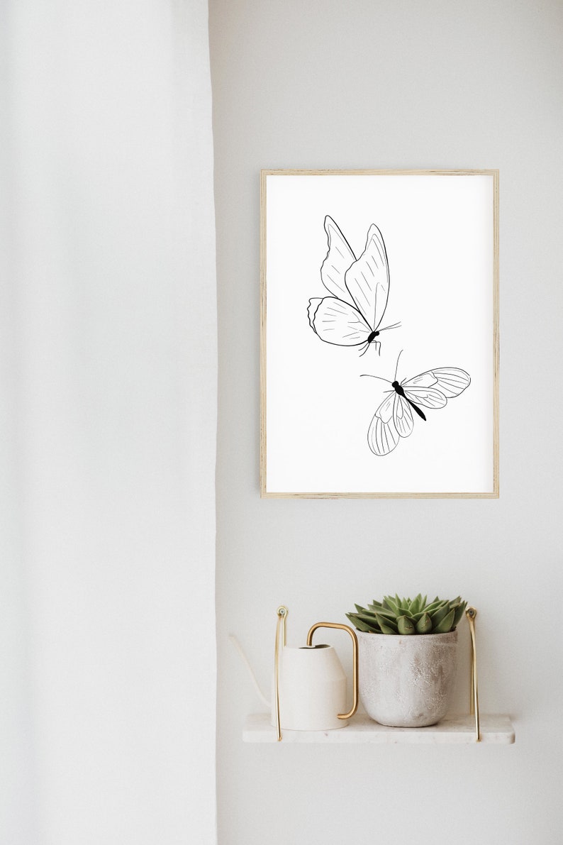May include: A black and white line drawing of two butterflies on a white background. The butterflies are in a simple, minimalist style. The drawing is framed in a light wood frame.