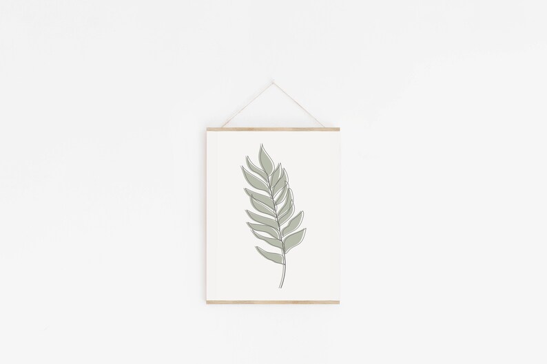 May include: A framed print of a single green leaf with a simple line drawing style. The leaf is hanging on a white wall.