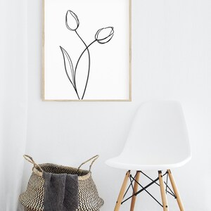 Puede incluir: Un dibujo en blanco y negro de dos tulipes en un marco de madera, colgado en una pared blanca. Una silla blanca con patas de madera se encuentra frente a una cesta tejida.