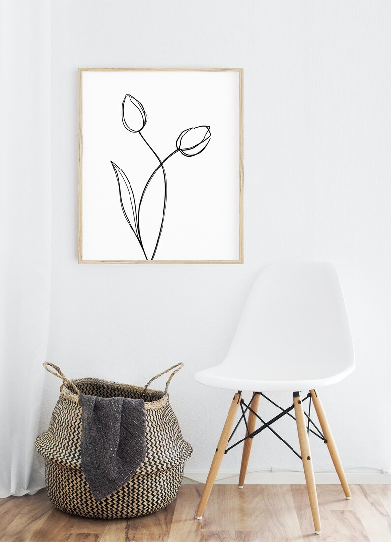 Puede incluir: Un dibujo en blanco y negro de dos tulipes en un marco de madera, colgado en una pared blanca. Una silla blanca con patas de madera se encuentra frente a una cesta tejida.