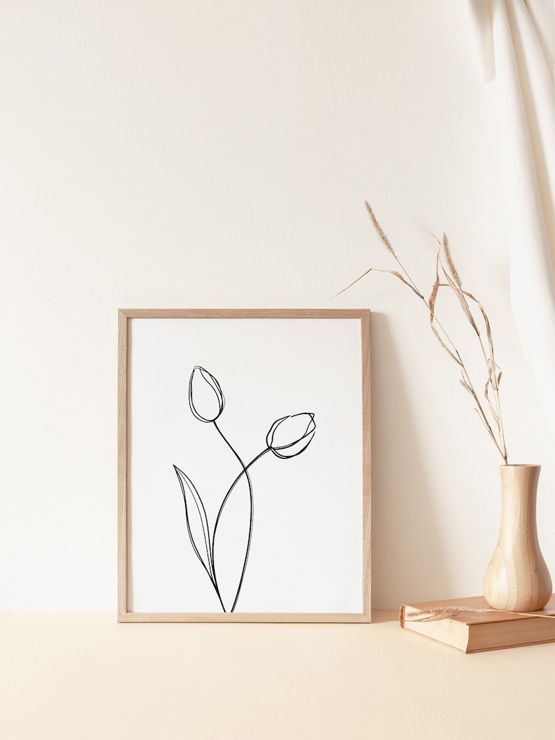 Puede incluir: Un dibujo en blanco y negro de dos tulipes en un estilo simple y minimalista. El dibujo est&aacute; enmarcado en un marco de madera clara y se encuentra sobre una superficie beige clara.