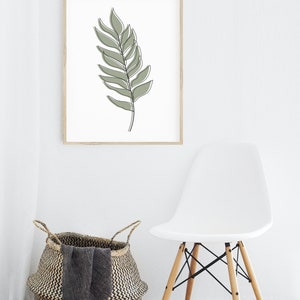 May include: A framed print of a single green leaf drawn in a minimalist style. The print is hanging on a white wall above a white chair and a woven basket.
