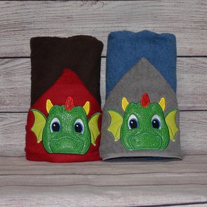 May include: Two hooded towels with a green dragon face embroidered on the front. One towel is red with brown trim and the other is gray with blue trim.