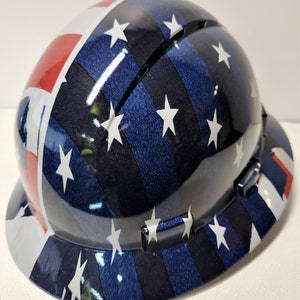 Könnte beinhalten: Glänzender Schutzhelm mit einem Design, das vom amerikanischen Flaggenmuster inspiriert ist. Der Helm hat ein blaues, weißes und rotes Farbschema mit weißen Sternen und Streifen. Geeignet für Bau- oder Industrieanwendungen.