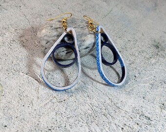 May include: A pair of blue and white teardrop-shaped earrings with a gold hook. The earrings are made of layered paper and have a delicate, intricate design.