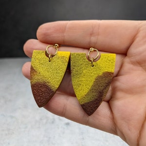 Könnte beinhalten: Ein Paar gelbe und braune geometrische Ohrringe mit goldenen Haken.