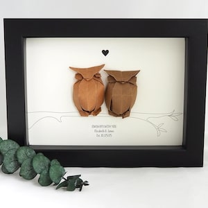 Könnte beinhalten: Gerahmtes Kunstwerk mit zwei Origami-Eulen auf einem Ast, darüber ein schwarzes Herz. Der Rahmen ist schwarz, der Hintergrund weiß. Text: "ALWAYS WITH YOU" und ein Datum.