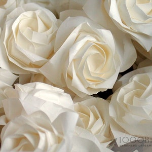 May include: A close-up of a bouquet of white origami roses. The roses are made of paper and are arranged in a cluster. The roses are all facing the same direction and are all the same size.
