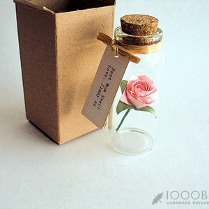 May include: A glass bottle with a cork stopper contains a pink origami rose. A small tag attached to the bottle reads "Best Mom Ever! Love, July 2012".