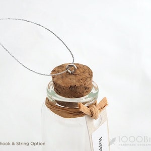 May include: A small glass bottle with a cork top and a silver eye hook. The bottle is tied with a brown string and has a white tag that says "Happy".