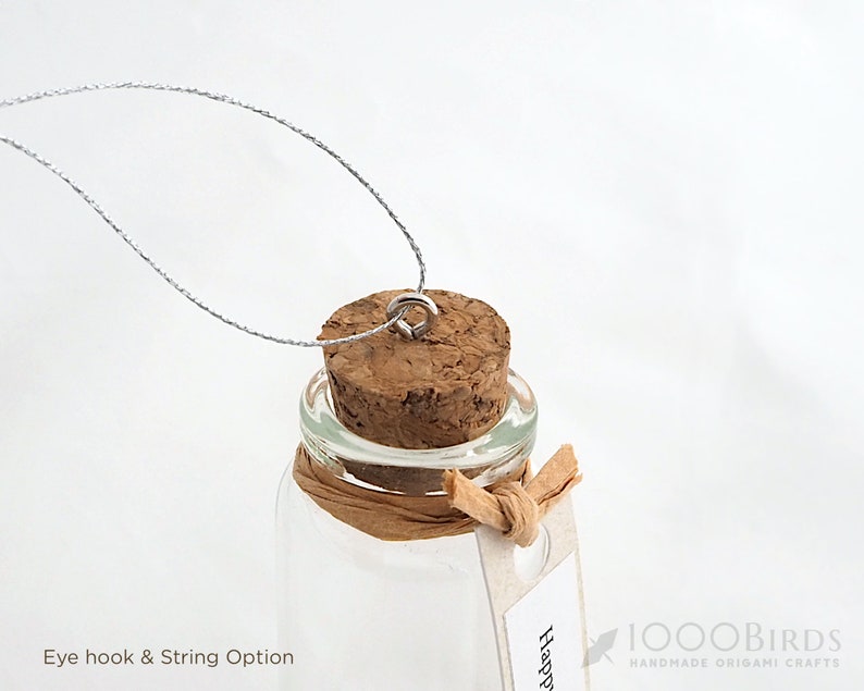 May include: A small glass bottle with a cork top and a silver eye hook. The bottle is tied with a brown string and has a white tag that says "Happy".