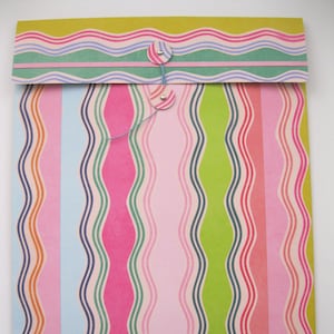 May include: A colorful envelope with a striped pattern of pink, green, blue, and orange. The envelope has a wavy design and is closed with two buttons.