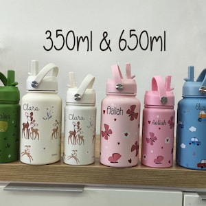 Könnte beinhalten: Eine Sammlung isolierter Wasserflaschen in verschiedenen Farben und Designs. Die Flaschen haben Namen und dekorative Muster, darunter Dinosaurier, Hirsche, Schmetterlinge und Autos. Größen: 350 ml und 650 ml. Jede Flasche hat einen Griff und einen Strohhalm.