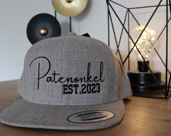 Op de afbeelding: Grijze baseballpet met zwarte borduurwerk dat "Patemonkel EST.2023" zegt.