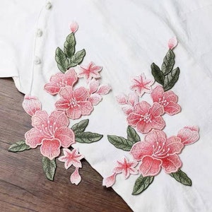 May include: Two pink and green embroidered floral appliques with delicate details. The appliques feature pink flowers with white centres and green leaves.