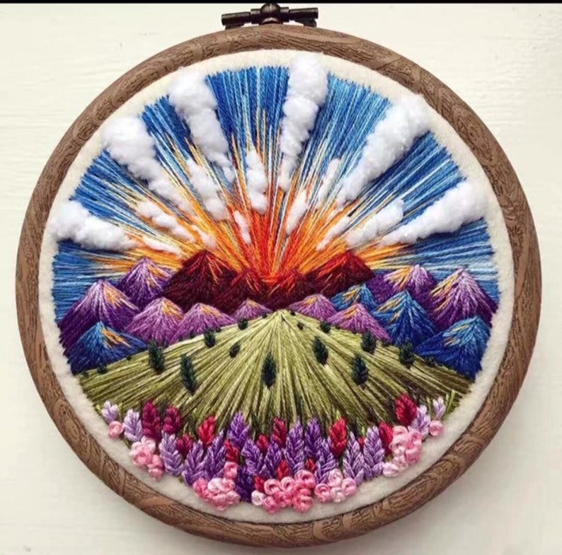 May include: A colorful embroidered hoop art piece depicting a sunset over a mountain range with purple and blue peaks, a green valley, and pink flowers at the bottom.