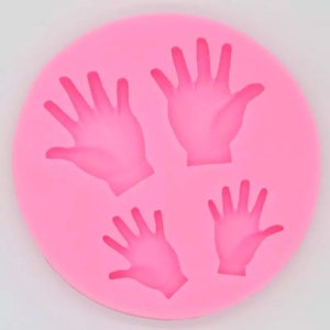 Könnte beinhalten: Rosa Silikonform mit vier Handformen. Die Form ist zum Herstellen von Fondant oder anderen essbaren Dekorationen gedacht.