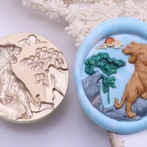 May include: A round, metal mould with a detailed design of a tiger standing on a rock with a tree and clouds behind it. The mould is used to create a resin or polymer clay charm.