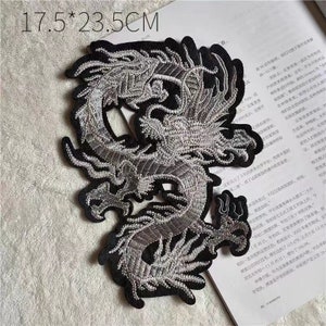 May include: A silver embroidered dragon patch on a black fabric background. The patch measures 17.5 inches by 23.5 inches.
