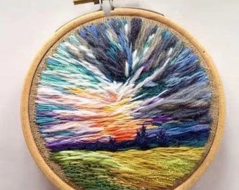 May include: A circular embroidery hoop with a colorful landscape scene. The scene features a sunset with a bright orange sky and a field of green grass. The embroidery is done with a variety of colored threads.