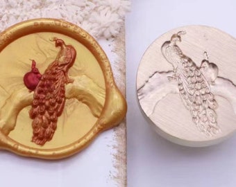 May include: A gold-coloured wax seal with a raised design of a peacock with a red pomegranate. The seal is next to a metal stamp with the same design.
