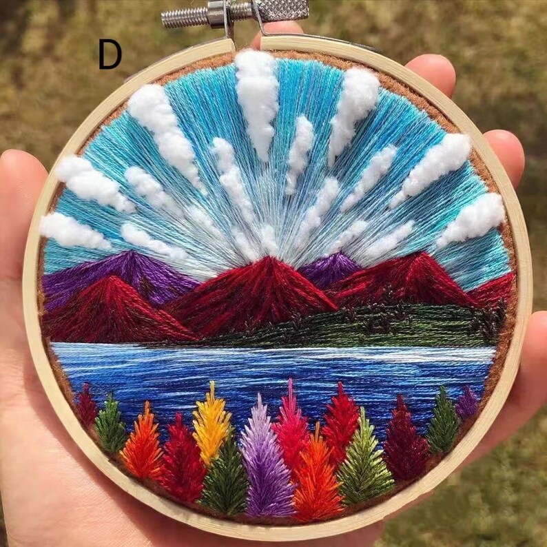 May include: Embroidered hoop art depicting a landscape with red mountains, a blue lake, green trees, and white clouds against a blue sky.
