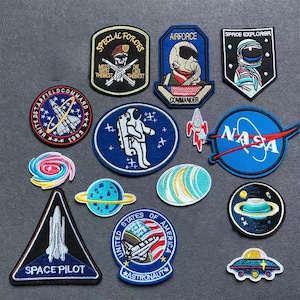 Könnte beinhalten: Eine Sammlung bestickter Aufnäher zum Thema Weltraum mit verschiedenen Motiven, darunter ein NASA-Logo, ein Astronaut, ein Space Shuttle, Planeten, eine Galaxie und militärische Abzeichen mit Texten wie Special Forces, Airforce und Space Pilot.