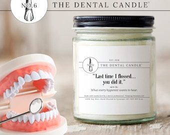 May include: A white candle in a clear glass jar with a black lid. The label reads "The Dental Candle" and features a tooth graphic. The text on the label reads "Last time I flossed... you did it." and "What every hygienist wants to hear."