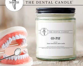 May include: A white candle in a clear glass jar with a black lid. The label reads "The Dental Candle" and "Co-Pay" with the tagline "smells like: Your insurance plan sucks." The candle is made with 100% soy wax and hand-poured in Syracuse, NY. The candle is 8 oz.